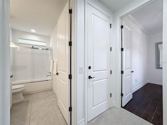 interior space featuring toilet, tile patterned floors, baseboards, ornamental molding, and bath / shower combo with glass door