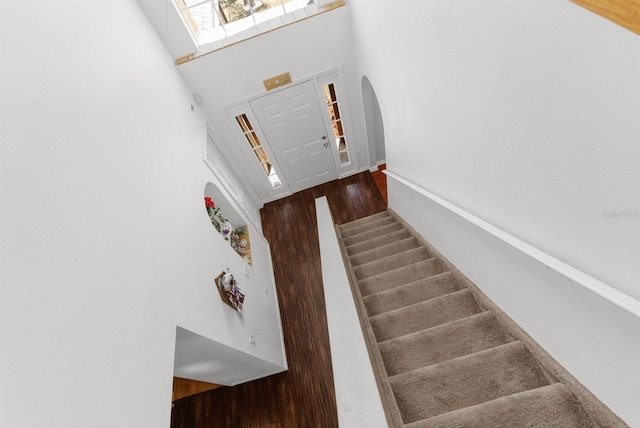 staircase with a towering ceiling, arched walkways, and wood finished floors