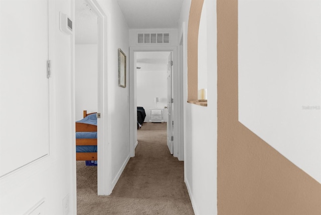 hallway with carpet floors, arched walkways, baseboards, and visible vents
