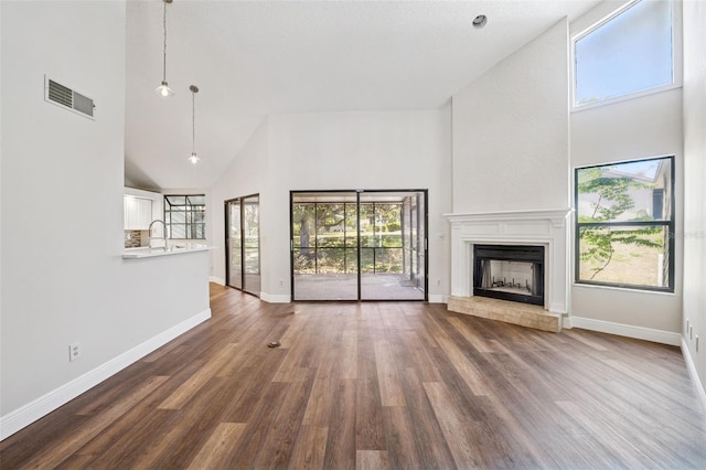 unfurnished living room with a fireplace with raised hearth, dark wood finished floors, visible vents, and high vaulted ceiling