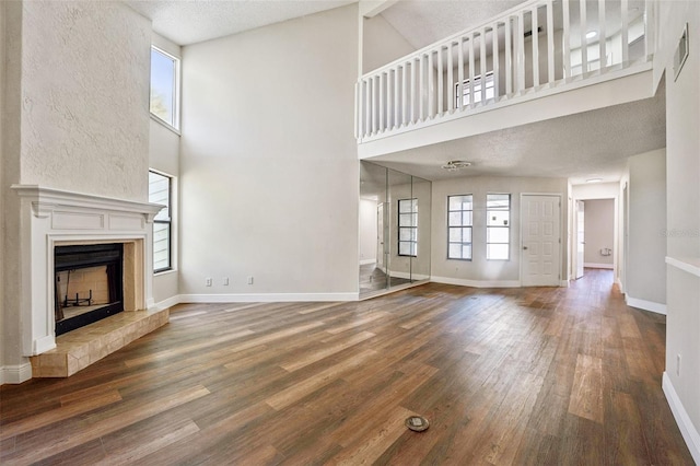 unfurnished living room featuring baseboards, wood finished floors, a high ceiling, and a fireplace with raised hearth