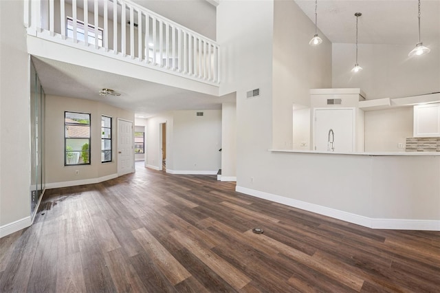 unfurnished living room featuring dark wood-style floors, a sink, visible vents, baseboards, and a high ceiling