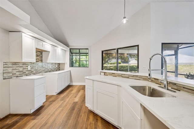kitchen featuring light wood finished floors, a sink, tasteful backsplash, vaulted ceiling, and white cabinetry