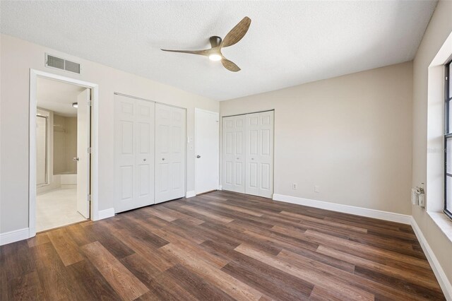 unfurnished bedroom featuring connected bathroom, multiple closets, baseboards, dark wood-style flooring, and visible vents