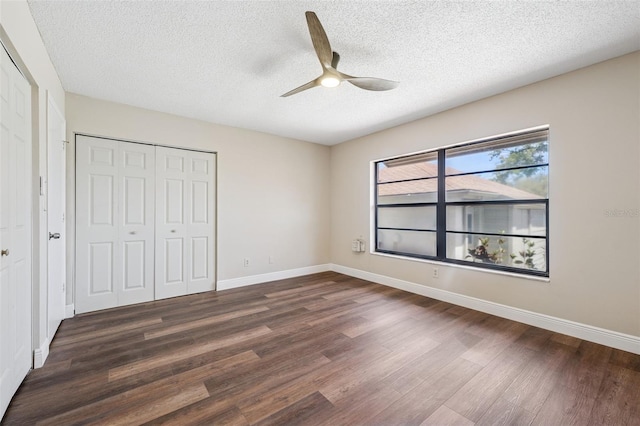 unfurnished bedroom with a textured ceiling, baseboards, a ceiling fan, a closet, and dark wood-type flooring