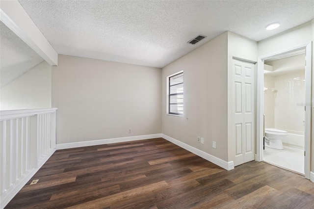 unfurnished bedroom featuring dark wood-style floors, visible vents, baseboards, a textured ceiling, and ensuite bathroom