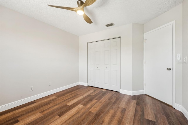 unfurnished bedroom featuring a textured ceiling, wood finished floors, a closet, baseboards, and visible vents