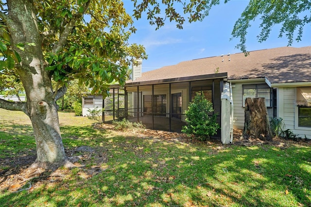 back of house featuring a lawn, a sunroom, a chimney, and a shingled roof