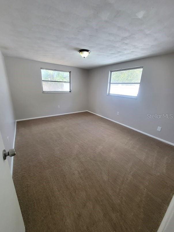 unfurnished room with plenty of natural light, baseboards, and dark carpet