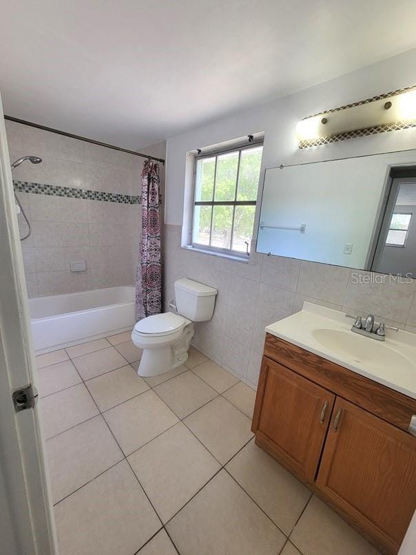 bathroom featuring tile walls, toilet, vanity, shower / bath combo with shower curtain, and tile patterned flooring