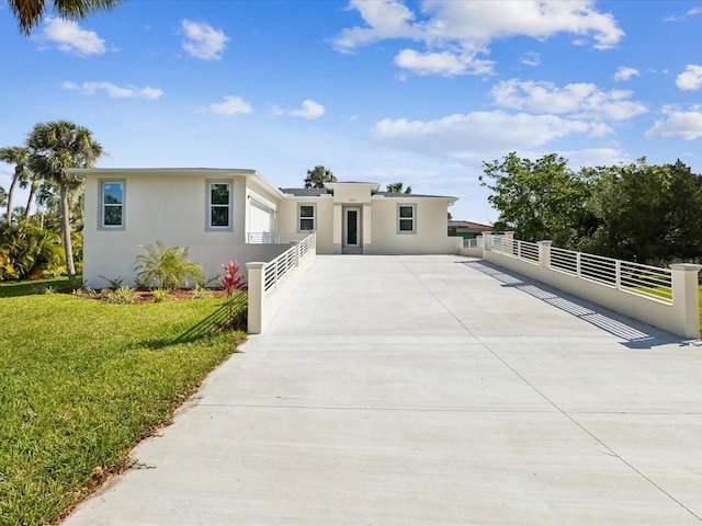 view of front of property featuring a front yard, driveway, stucco siding, and fence