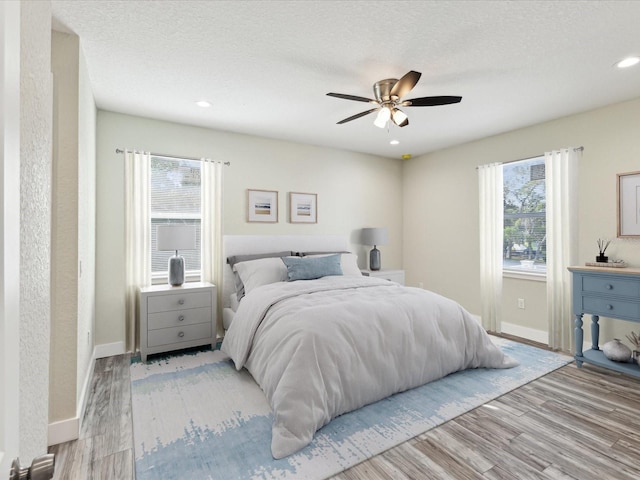 bedroom featuring baseboards, a textured ceiling, ceiling fan, and light wood finished floors