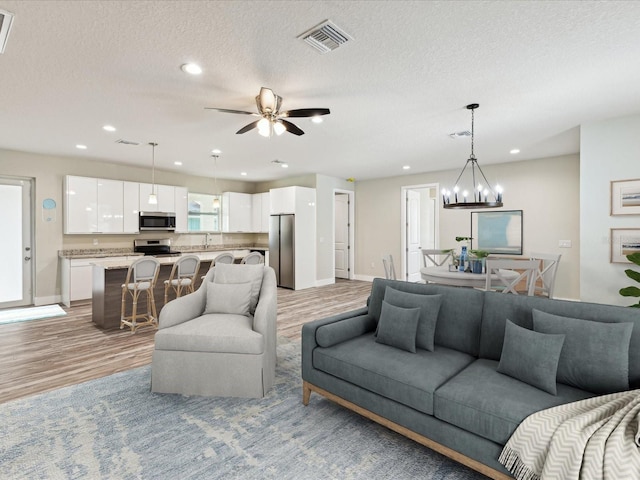 living room featuring a textured ceiling, visible vents, recessed lighting, and light wood finished floors