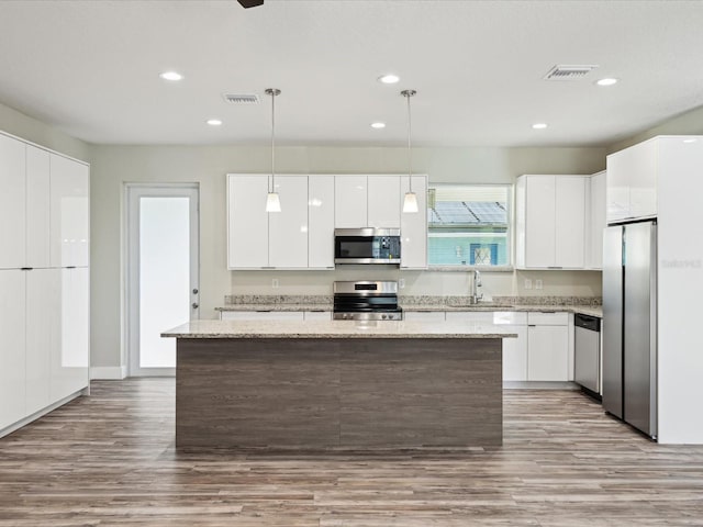 kitchen with visible vents, appliances with stainless steel finishes, white cabinetry, a sink, and a center island