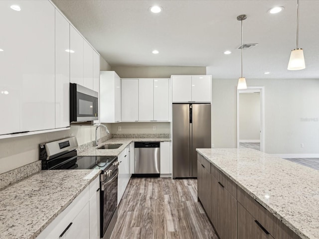 kitchen with a sink, modern cabinets, stainless steel appliances, visible vents, and light wood-style floors