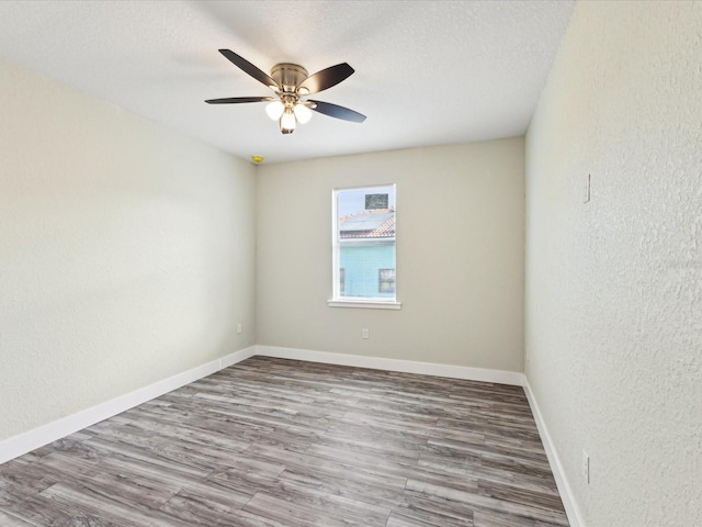 spare room with a textured wall, a textured ceiling, baseboards, and wood finished floors