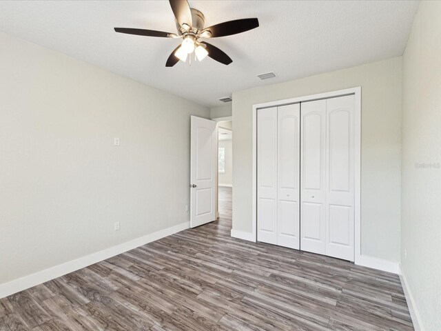 unfurnished bedroom with a closet, visible vents, baseboards, ceiling fan, and wood finished floors