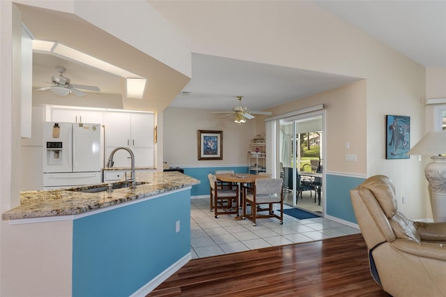 kitchen featuring white fridge with ice dispenser, ceiling fan, a sink, light wood-style floors, and light stone countertops