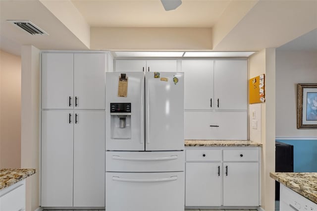 kitchen featuring white fridge with ice dispenser, white cabinetry, and light stone counters
