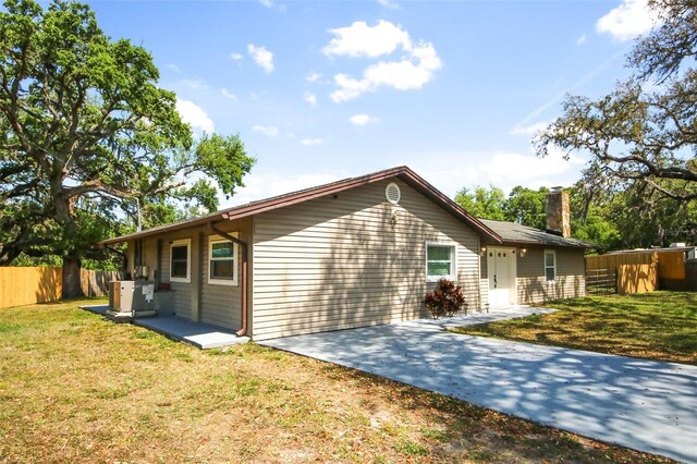 view of property exterior with cooling unit, concrete driveway, fence, a lawn, and a chimney