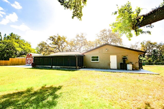 back of house with stucco siding, an outbuilding, fence, a storage unit, and a lawn