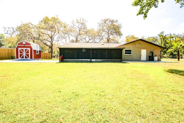 rear view of house featuring a lawn, an outbuilding, fence, and a sunroom