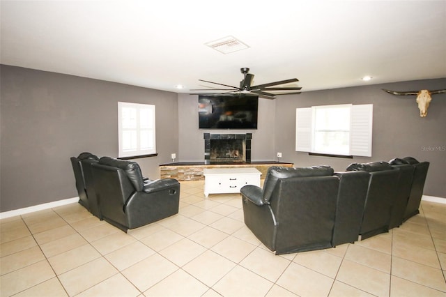 living room featuring light tile patterned flooring, visible vents, baseboards, a fireplace with raised hearth, and a ceiling fan