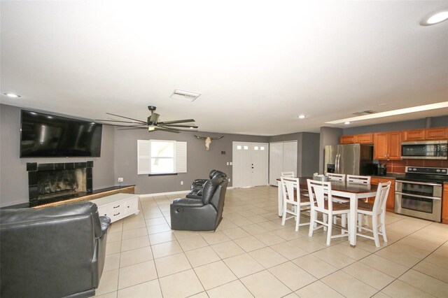 living room with light tile patterned flooring, a fireplace with raised hearth, visible vents, and ceiling fan