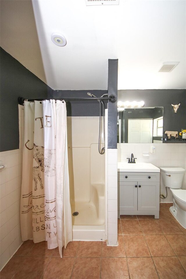 bathroom with a stall shower, tile patterned floors, toilet, vanity, and tile walls