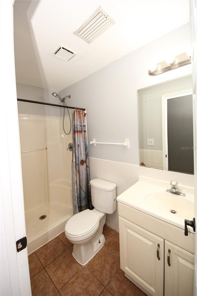 bathroom with tile walls, visible vents, toilet, curtained shower, and tile patterned flooring