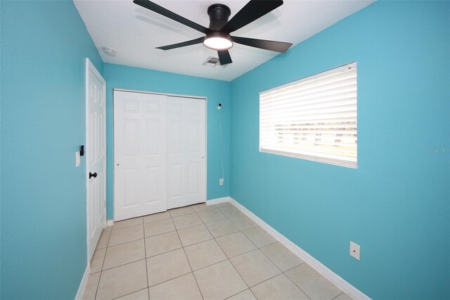 unfurnished bedroom featuring light tile patterned floors, baseboards, visible vents, a ceiling fan, and a closet