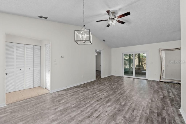 unfurnished living room featuring ceiling fan with notable chandelier, baseboards, wood finished floors, lofted ceiling, and visible vents