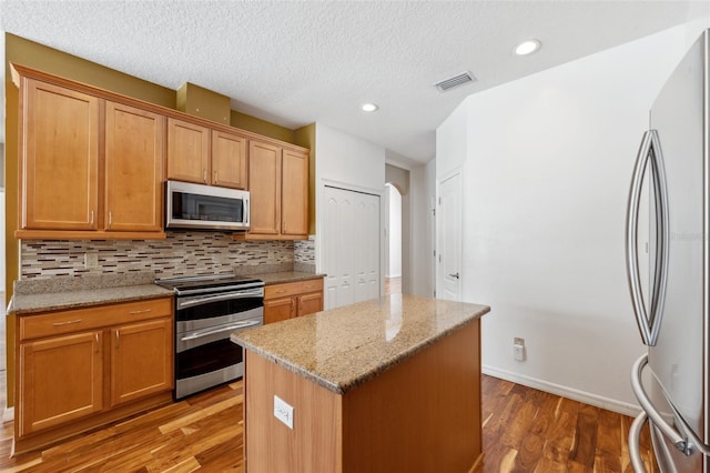 kitchen with appliances with stainless steel finishes, a center island, wood finished floors, backsplash, and visible vents