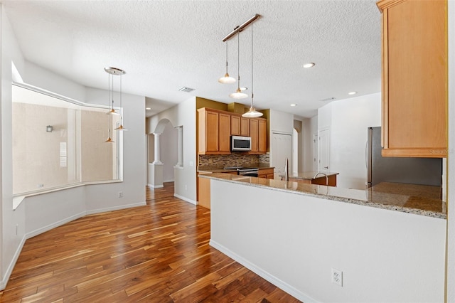 kitchen with a textured ceiling, stainless steel appliances, wood finished floors, backsplash, and visible vents
