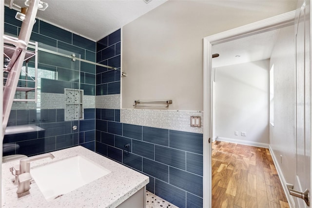 full bath with tile walls, a tile shower, wood finished floors, and vanity