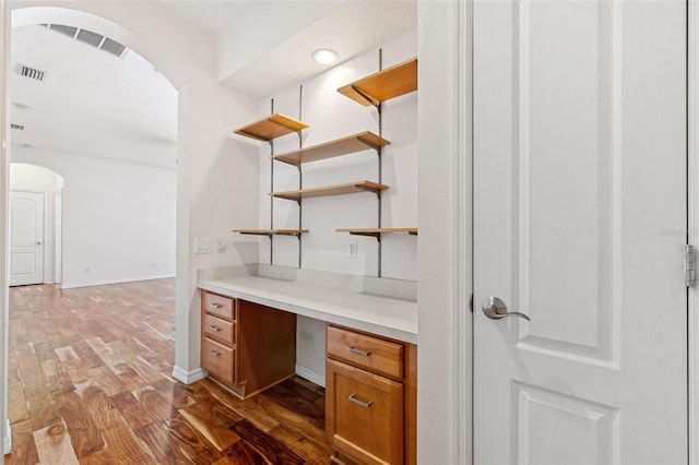 unfurnished office featuring built in desk, arched walkways, visible vents, and wood finished floors