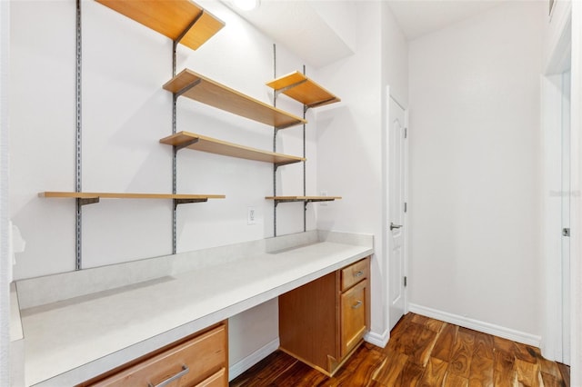 unfurnished office featuring baseboards, dark wood-style flooring, and built in desk