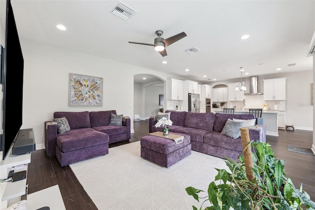living room featuring a ceiling fan, visible vents, arched walkways, and dark wood-type flooring