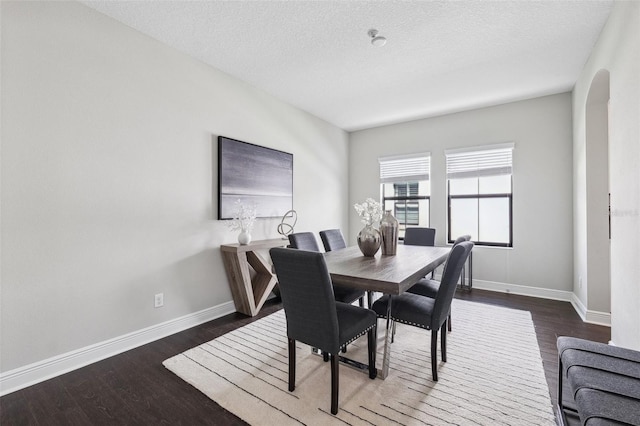 dining area with baseboards, arched walkways, a textured ceiling, and dark wood-style flooring