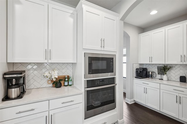 kitchen with white cabinets, oven, arched walkways, built in microwave, and tasteful backsplash