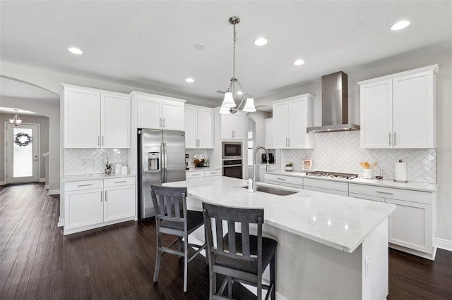 kitchen with wall chimney range hood, tasteful backsplash, a sink, arched walkways, and appliances with stainless steel finishes