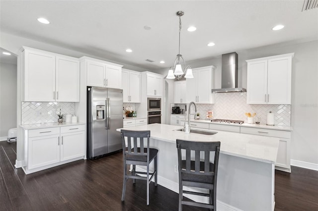 kitchen with dark wood-style floors, a sink, tasteful backsplash, wall chimney range hood, and appliances with stainless steel finishes