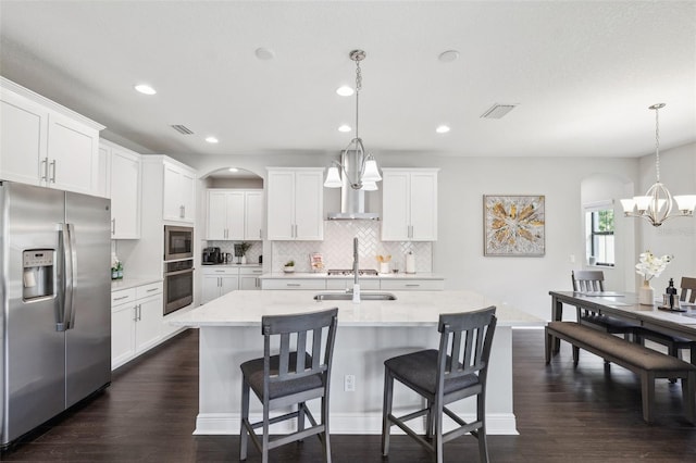 kitchen with stainless steel appliances, backsplash, a sink, arched walkways, and a notable chandelier