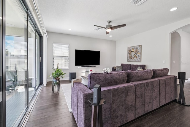 living area with visible vents, dark wood-style floors, arched walkways, and ceiling fan