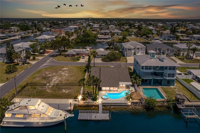 aerial view at dusk of a residential view, a water view, and view of pool