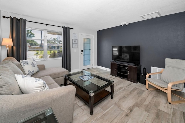 living area with baseboards, light wood finished floors, and visible vents