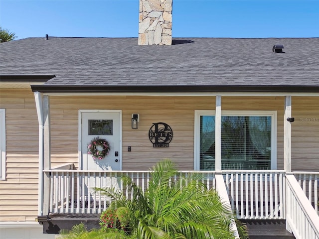 entrance to property with a porch, a shingled roof, and a chimney