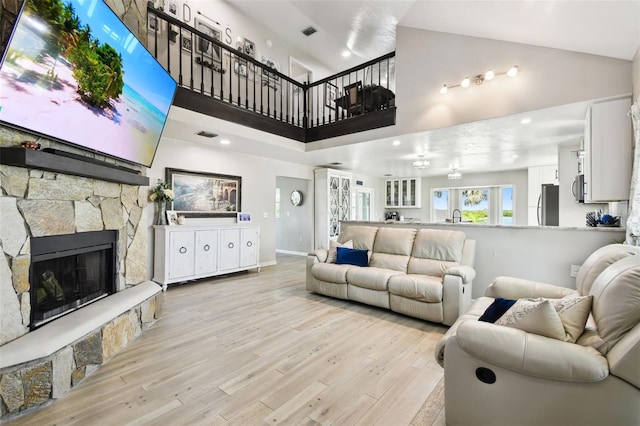 living room with visible vents, light wood-style flooring, a stone fireplace, and high vaulted ceiling