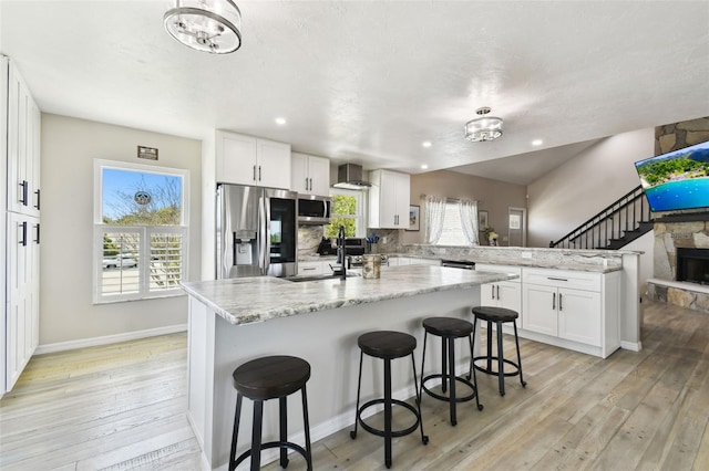 kitchen with white cabinetry, a sink, a peninsula, stainless steel appliances, and light wood-style flooring