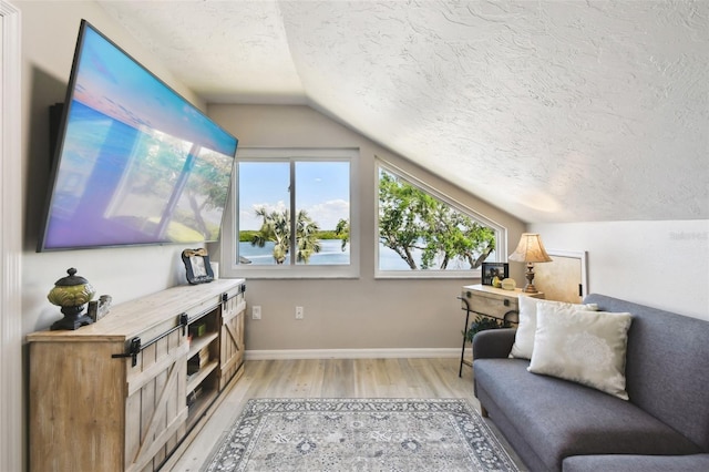 interior space with lofted ceiling, a textured ceiling, baseboards, and light wood-style floors